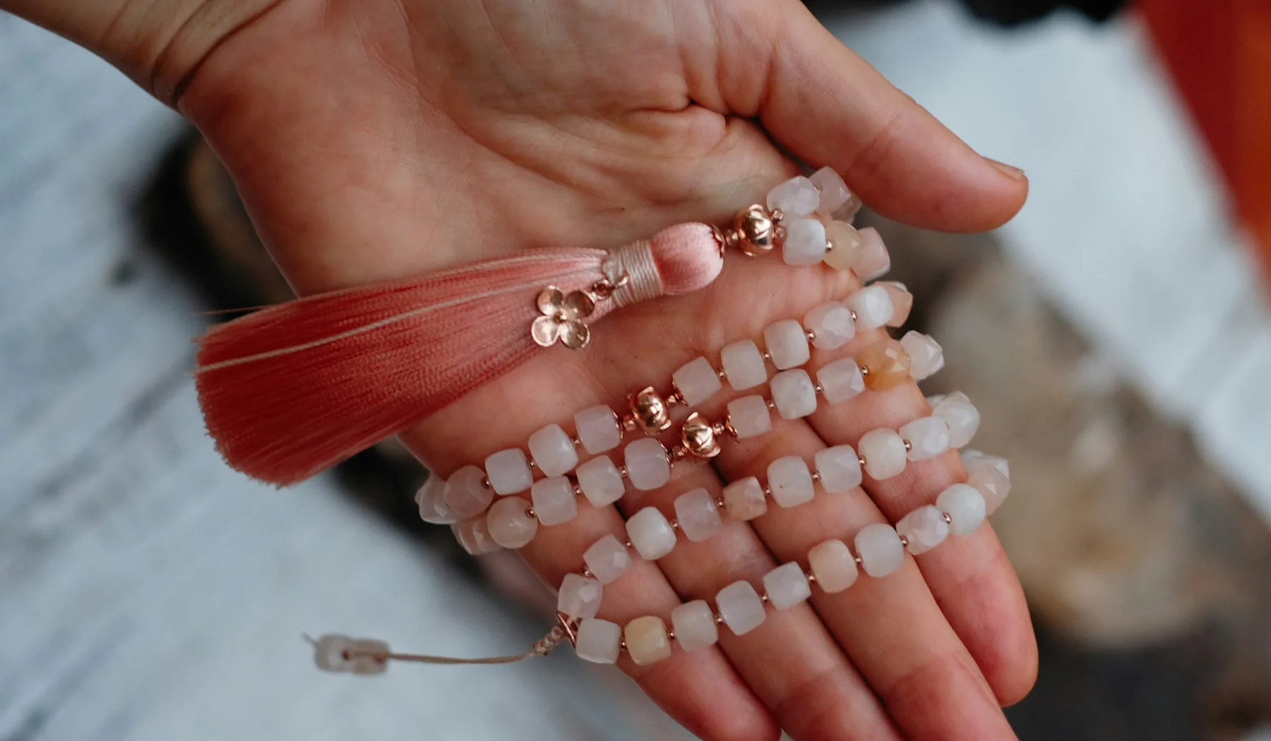 Hands holding a pale beaded necklace with a fabric tassel