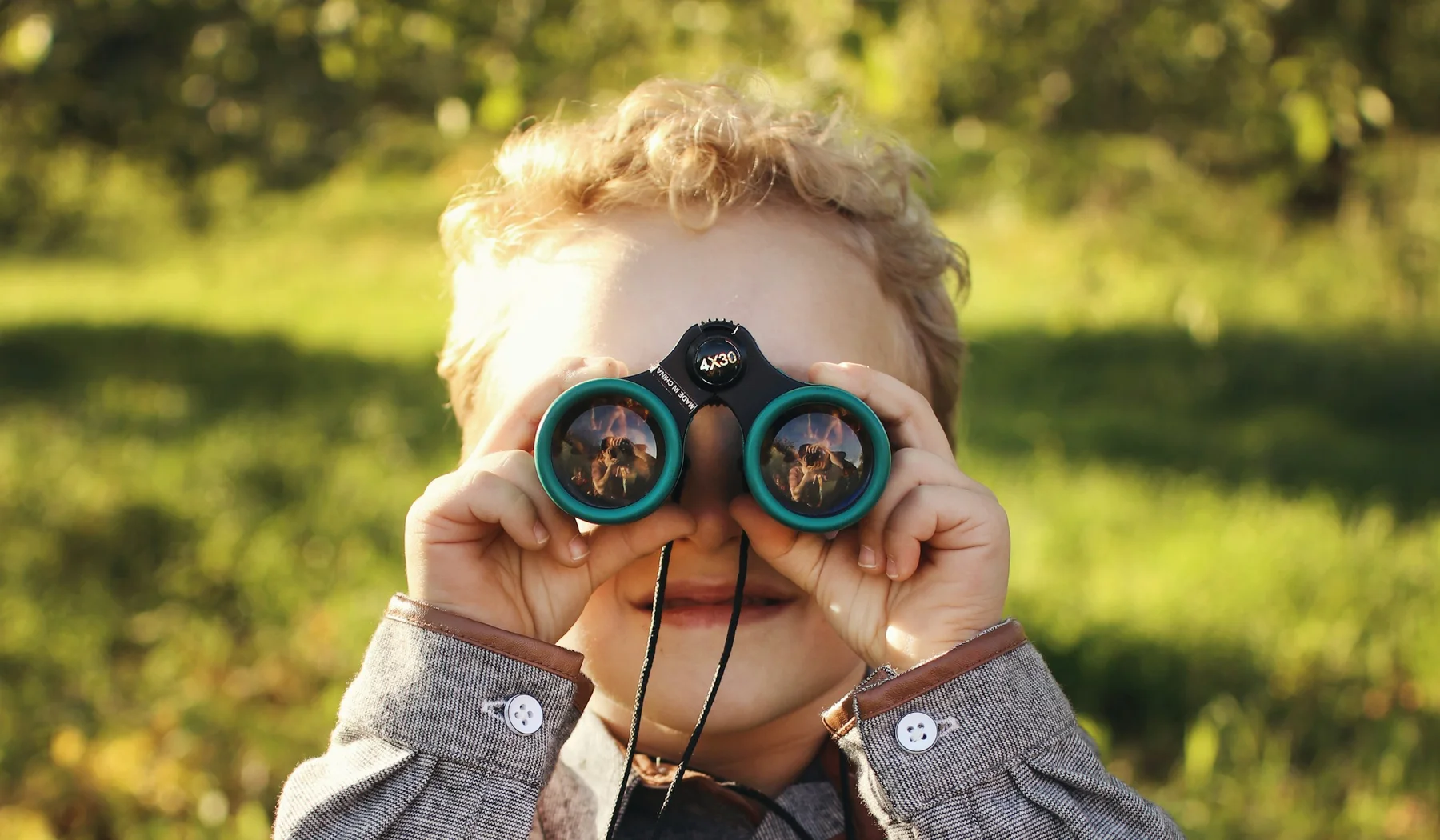 Young child looking through green binoculars outdoors