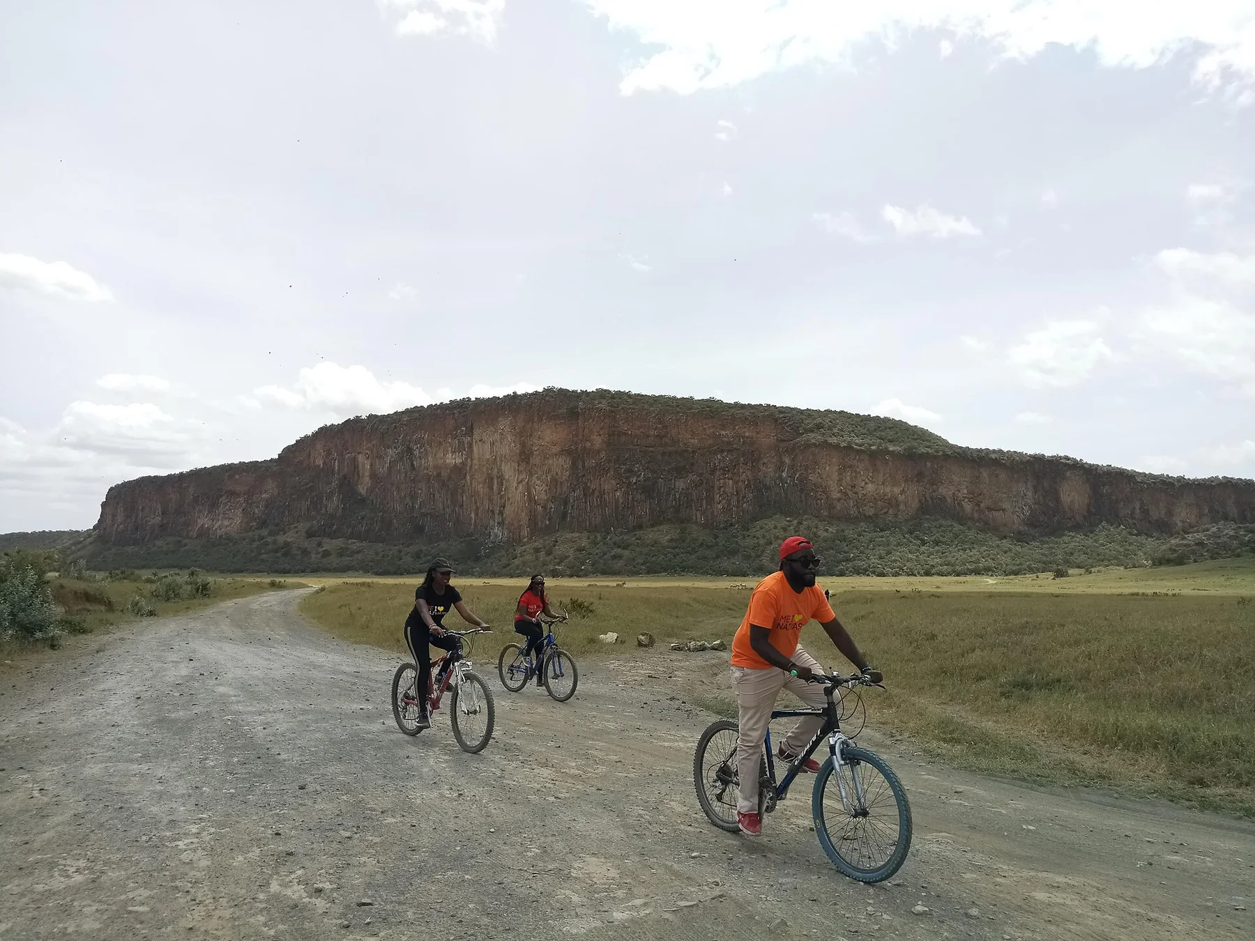 Three travellers cycling on a gravel road beneath the cliffs in Hell's Gate National Park