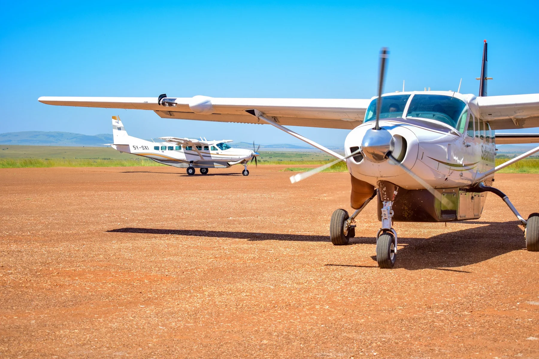 Two light aircraft on a dirt airstrip in the Maasai Mara