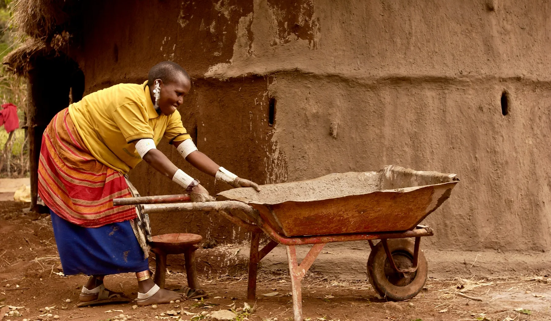 Woman using a wheelbarrow beside an earthen building