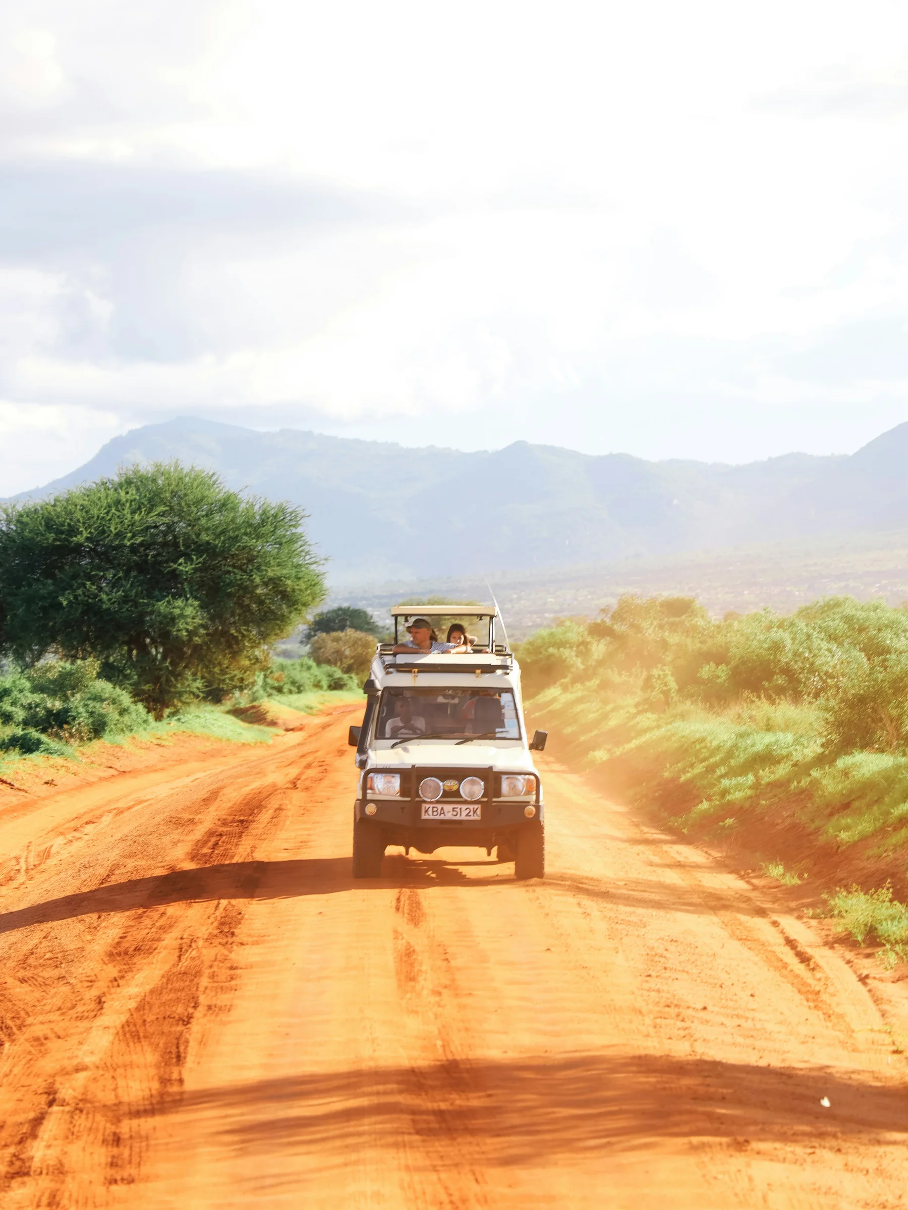 Safari vehicle driving along a red-earth road in Kenya