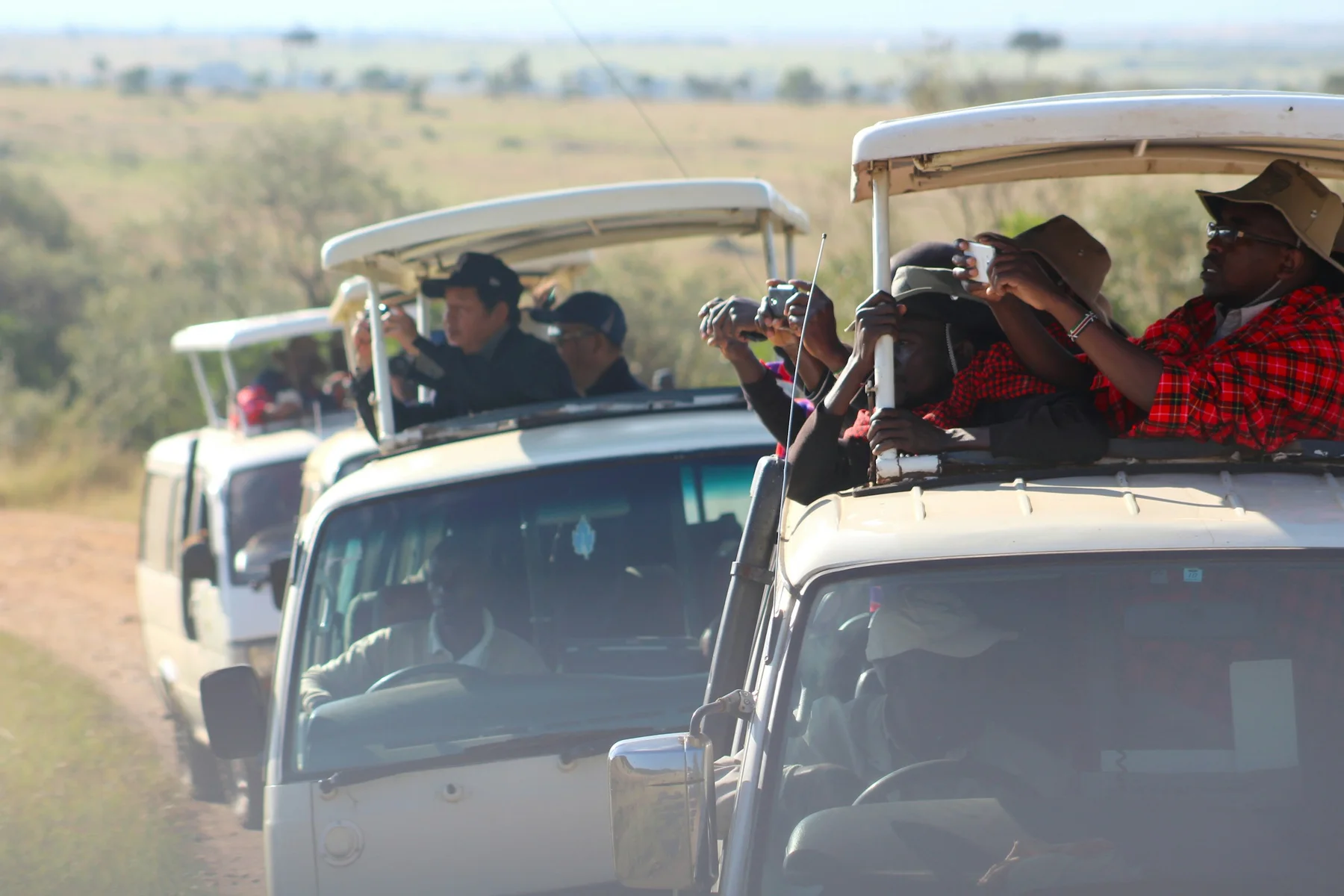 Several open-roof safari vehicles stopped on a Masai Mara track while guests photograph wildlife